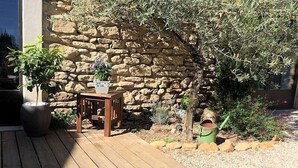 Une terrasse en bois avec un muret en pierre, une petite table, des plantes en pot et un seau vert.
