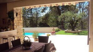 Une terrasse extérieure avec une table à manger, des chaises et une vue sur une piscine et un jardin.