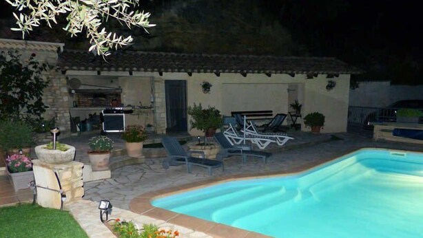 Une piscine bordée de pierres, entourée de plantes en pot et d’une pelouse.