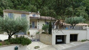 Une maison à deux étages avec une façade en pierre, une voiture garée dans le garage et un arbre dans le jardin.