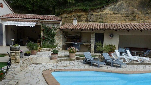 Une piscine en pierre, entourée de chaises longues, de plantes en pot et d’un mur de pierre.