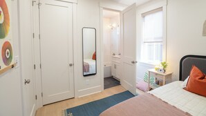 A bedroom with a bed, a bedside table with a lamp, a window, and a bathroom visible through an open door. - PatioPad~UltraWalkable~Fenced~Pets~Design2Delight! (Raleigh)