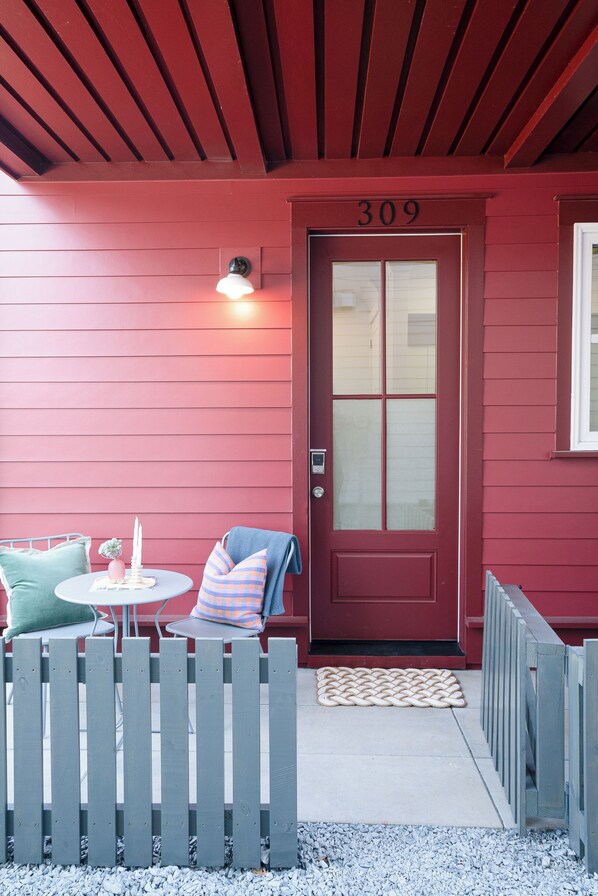 Une porte rouge portant le numéro 309, une petite table avec une chaise et une clôture en bois.