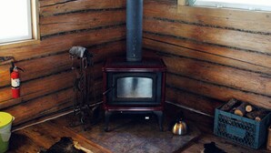 Een eenvoudig houten blokhut interieur met houten wanden, een houtkachel, een brandblusser en een raam.