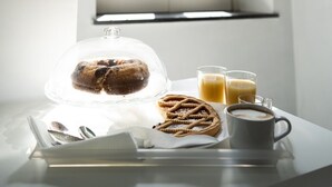 A breakfast setting with a pastry under a glass dome, two glasses of orange juice, and a cup of coffee on a table near a window with white shutters. - San Felice Palace (Naples)