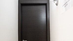 A dark wooden door with a silver handle and a keyhole, a white wall, and a sign with text. - San Felice Palace (Naples)