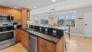 A spacious kitchen with wooden cabinets, stainless steel appliances, a large island with a black countertop, and a view of the outdoors through large windows.