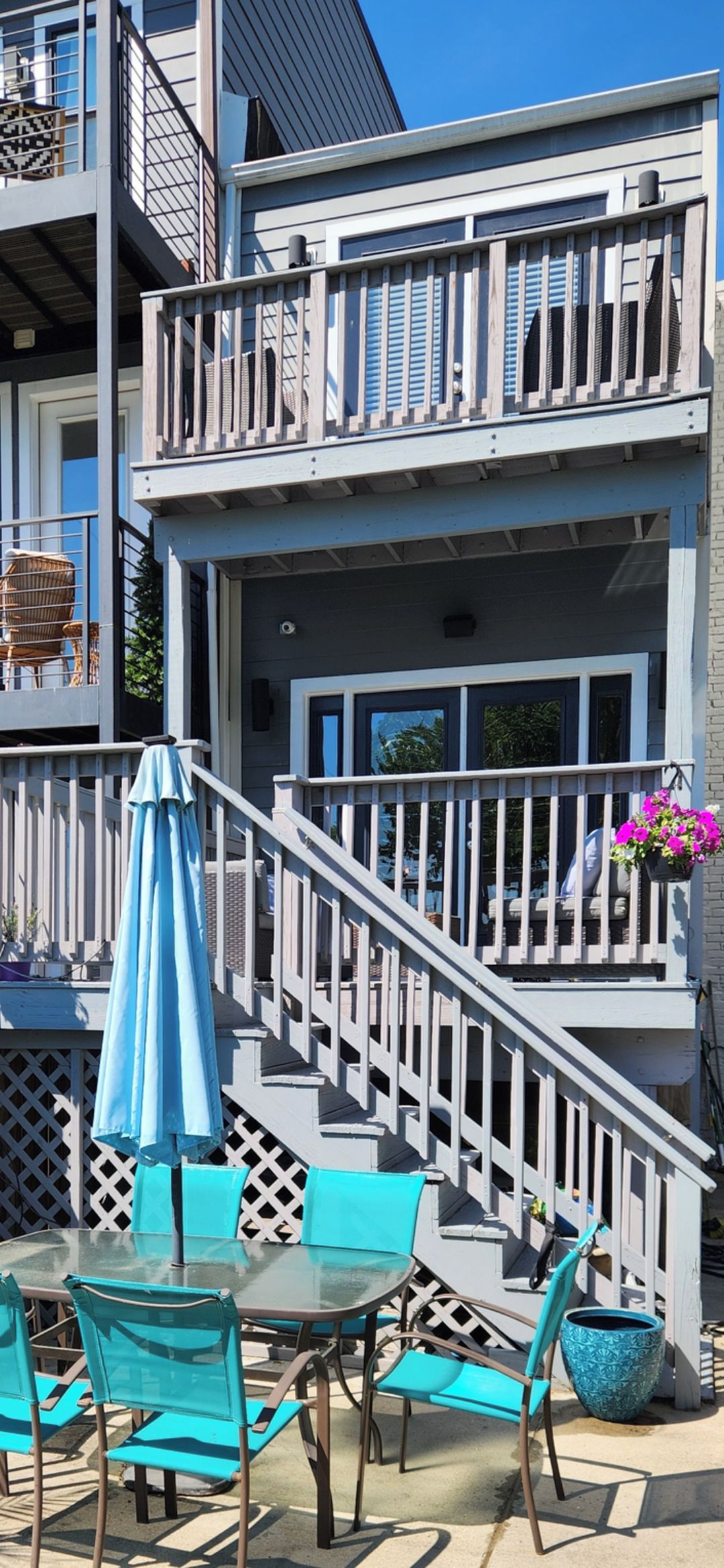 A multi-story building with a balcony, outdoor seating area with chairs and a table, and a staircase leading to the upper levels.