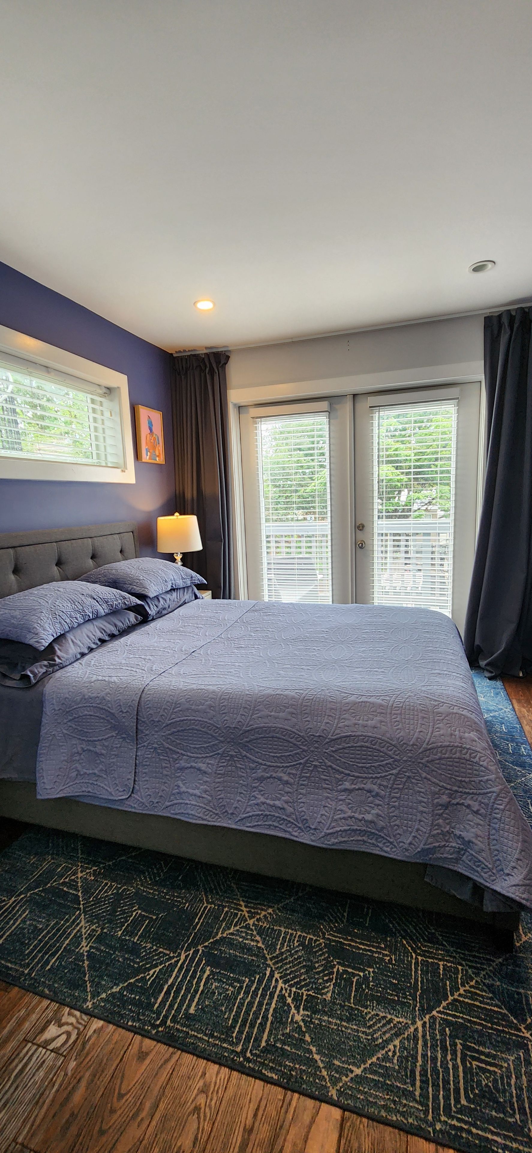 A bedroom with a large bed, a nightstand, a lamp, and a view of the outdoors through the window.