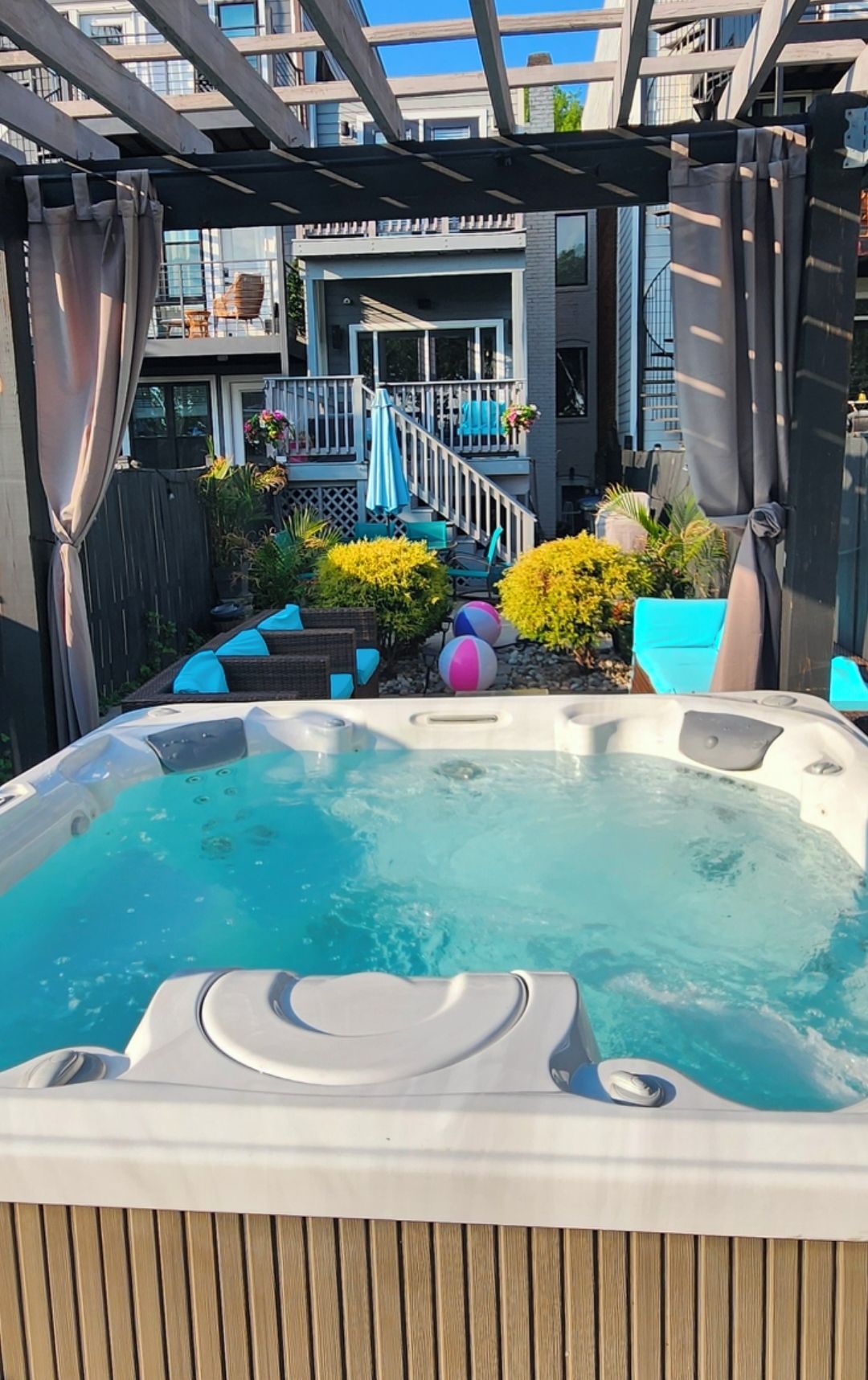 A hot tub with a wooden deck and a staircase leading to a balcony.