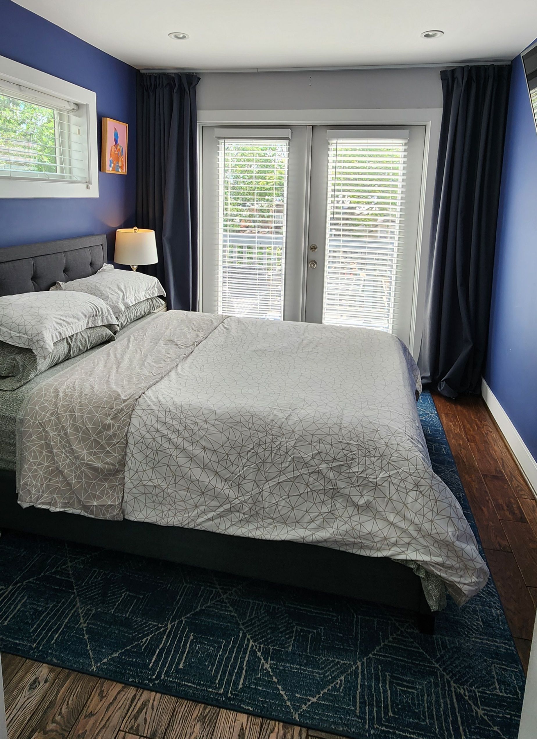 A bedroom with a bed, a nightstand, a lamp, and a window with blinds.