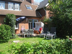 Une maison en briques avec un patio couvert, du mobilier d’extérieur et un jardin.
