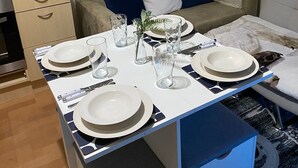 Een knus woongedeelte met een eettafel voor vier personen, een bank, een koffiezetapparaat en een klein plantenrek.