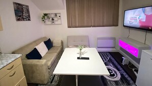Een moderne woonkamer met een witte tafel, een beige bank en een aan de muur bevestigde televisie.