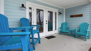 A covered porch with turquoise Adirondack chairs, a white door with glass panels, and a small table.