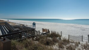 A beach with a wooden boardwalk leading to the shore, a signpost, and a sandy beach area.