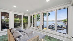 A sunroom with large windows overlooking a lake, wicker furniture, and a stone-tiled floor. - Lakeside Living - Firepit, Outdoor Fireplace, Kayaks, Arcade and much more! (Sherrills Ford)
