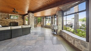 A covered patio area with stone walls, a stone fireplace, wicker furniture, and a view of the outdoors. - Lakeside Living - Firepit, Outdoor Fireplace, Kayaks, Arcade and much more! (Sherrills Ford)
