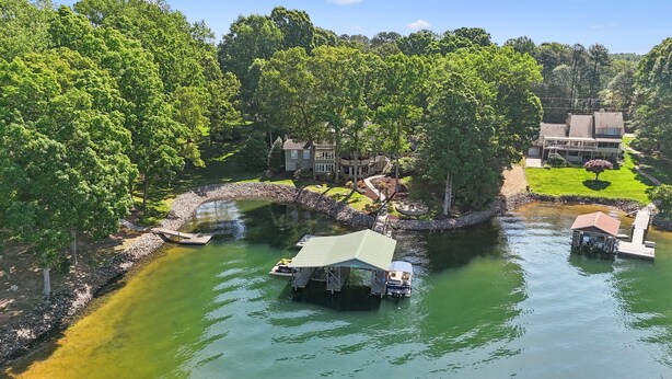 A lakeside property with a dock, a small boat, and a house with a large deck. - Lakeside Living - Firepit, Outdoor Fireplace, Kayaks, Arcade and much more! (Sherrills Ford)