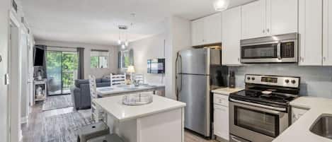 A modern kitchen with stainless steel appliances, a central island, and a dining area with a sofa and table.