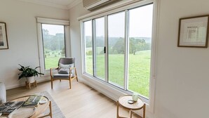 Una habitación con ventanas amplias, una silla, una mesita y una planta.