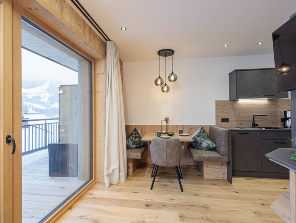 A modern kitchen with wooden cabinets, a dining area with a table and chairs, and a view of a snowy landscape through large windows.