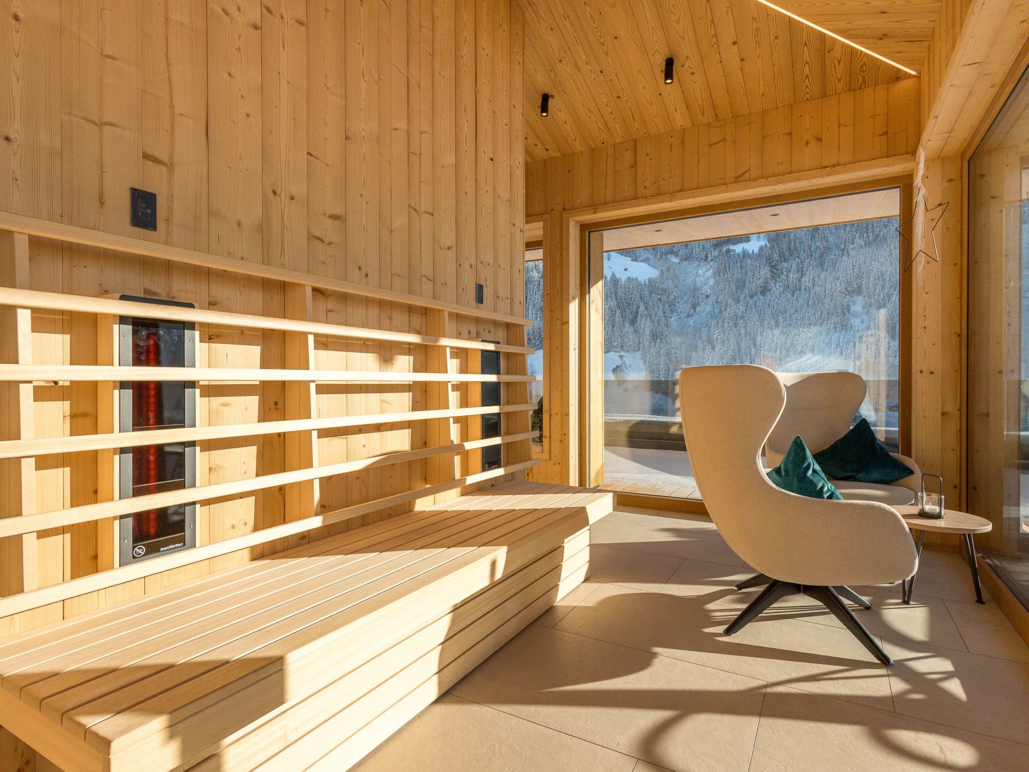 A wooden interior with a bench, a chair, and a large window offering a snowy landscape view.