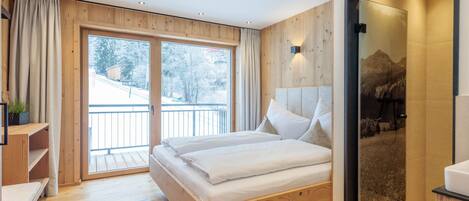 Une chambre moderne avec un lit en bois, un balcon et une vue sur des arbres enneigés.