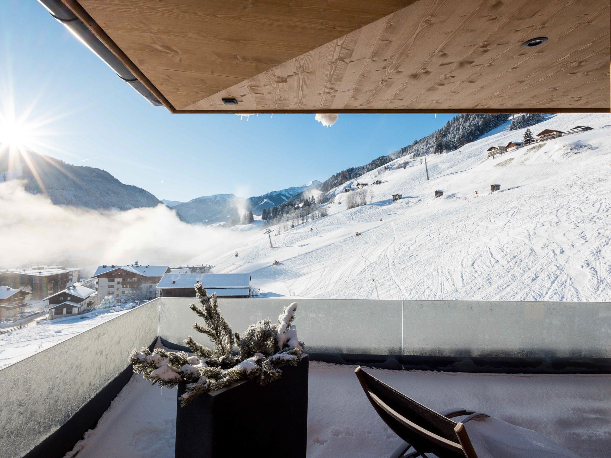 Un balcón con vistas a un paisaje nevado de montañas, que incluye una pista de esquí y edificios.