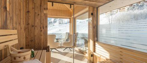 A wooden cabin with a sauna, a wooden bench, and a view of a snowy landscape.