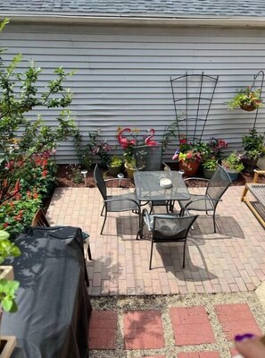Une terrasse avec une table et des chaises, entourée de plantes en pot et d’une clôture en métal.