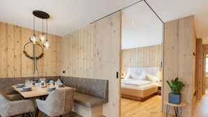 Un interior moderno con una pared de madera, un comedor con mesa y sillas, una cama con cabecero blanco y una pequeña planta sobre una mesita.