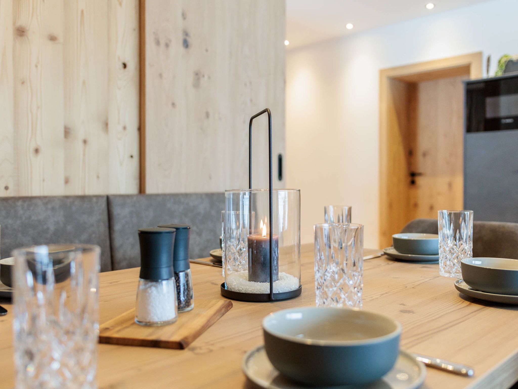 Une table de salle à manger en bois, agrémentée de salières et de poivrières, d’un chandelier et de verres transparents.