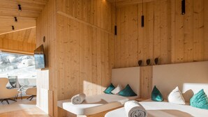 Een moderne hotelkamer met houten paneelwanden, een groot bed, een kleinere zithoek en een televisie aan de muur, met uitzicht op een besneeerd landschap.