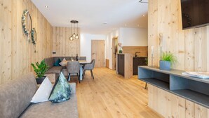 Ein modernes Wohnzimmer mit Holzboden, einer Couch, einem Esstisch mit Stühlen und einer Küchenzeile mit Holzschränken.