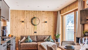 Een moderne woonkamer met een houten wand, een bank en een eethoek met een tafel gedekt voor twee personen.