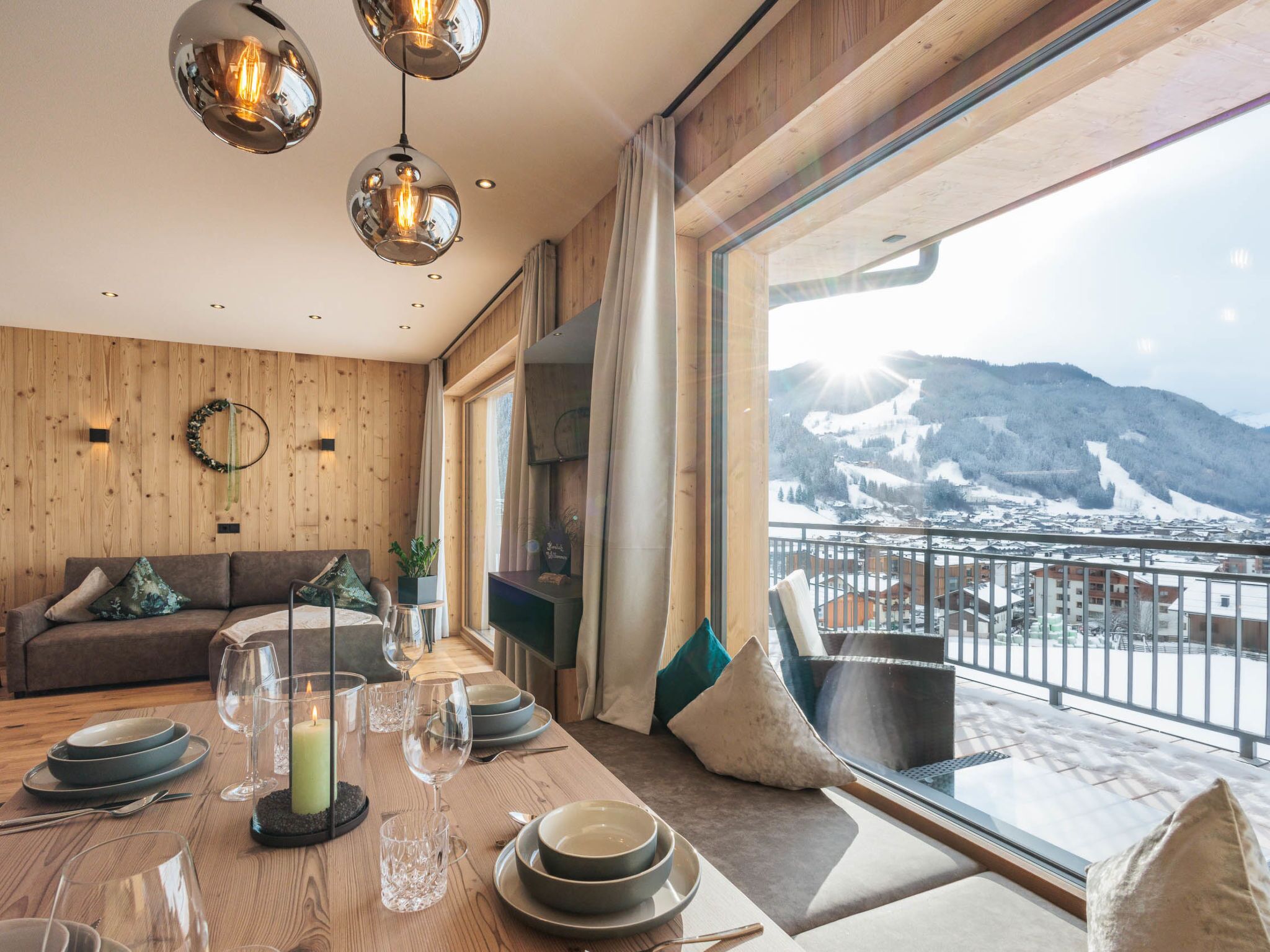 A modern dining area with a wooden table set for a meal, a sofa, and a view of a snowy mountain landscape.