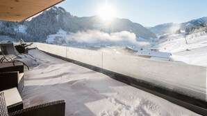 Un balcone imbiancato dalla neve con mobili in vimini, affacciato su un paesaggio montano innevato e una pista sciistica.