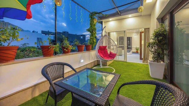 Una terraza en la azotea con mesa de vidrio, sillas de mimbre, plantas en macetas y un sillón colgante.