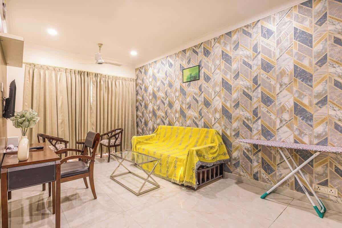 Un salon avec un canapé recouvert d’un tissu jaune, une table à manger avec des chaises et un mur orné d’un motif.