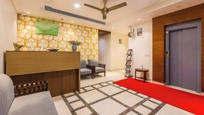 A hotel reception area with a wooden reception desk, a red carpet, a ceiling fan, and a wall-mounted clock. - Nature-inspired luxury 1 BHK (Gurugram)