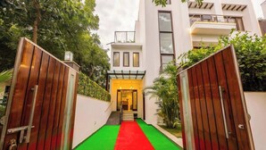 A modern building with a red carpet leading to a yellow entrance, surrounded by greenery. - Nature-inspired luxury 1 BHK (Gurugram)