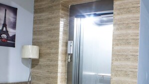 A modern elevator with a metallic finish, a wall-mounted telephone, and a floor lamp in a lobby area. - Tranquil 2BHK Oasis in the Heart of Gurugram (Gurugram)
