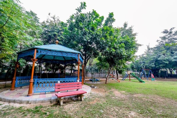 A gazebo with a blue roof and ornate design, surrounded by a grassy area and trees.