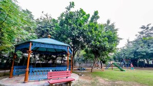 A gazebo with a blue roof and ornate railings, surrounded by a grassy area and trees. - Eco-chic haven in Gurgaon with balcony (Gurugram)