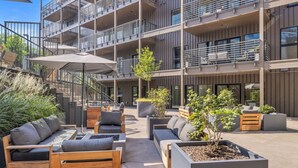 An outdoor seating area with modern furniture and planters, surrounded by a multi-story building with balconies. - Diamonds Are Forever, Ultimate Bachelorette Pad! Walk to Broadway! Pool. Gym, Parking & More (Nashville)