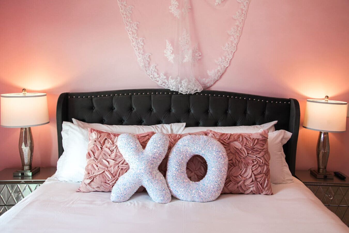 A bed with a large 'XO' pillow, a tufted headboard, and two bedside lamps.