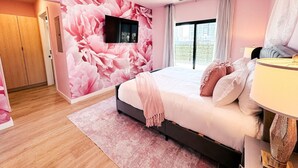 A bedroom with a large bed, a TV mounted on the wall, and a window with curtains. - Diamonds Are Forever, Ultimate Bachelorette Pad! Walk to Broadway! Pool. Gym, Parking & More (Nashville)