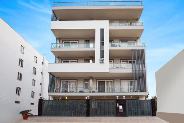 Un immeuble résidentiel à plusieurs étages, doté de balcons, d’une entrée sécurisée et surplombant un ciel dégagé.