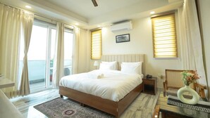 Habitación de hotel con una cama grande, ventilador de techo, mesita de noche, una silla, mesa de comedor y ventana con persianas.